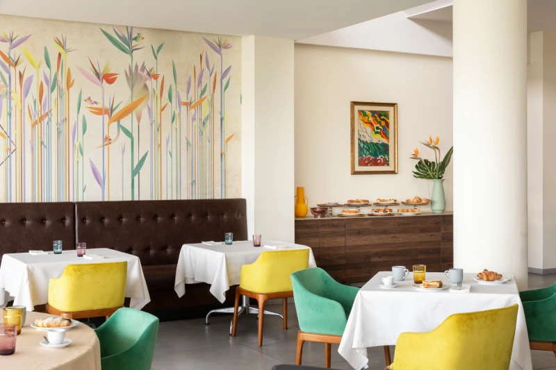 Bright breakfast room with colorful chairs, floral mural and buffet, ideal for stays in Sarzana, Liguria - Hotel Al Sant'Andrea, BZAR hotels in Liguria